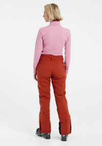 Maglietta rosa a maniche lunghe e pantaloni da sci arancioni imbottiti con cerniere alle caviglie, su uno sfondo bianco semplice.
