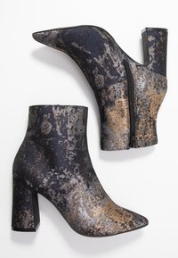 Bottines noires et dorées en tissu texturé, à bout pointu et talon épais ; elles présentent un détail de fermeture éclair sur le côté.