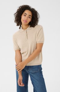 Beige polo shirt met korte mouwen, een kraag en drie knopen, gemaakt van zacht materiaal, gecombineerd met blauwe denim jeans.