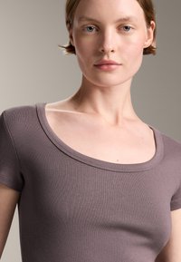 Top cu mânecă scurtă din material ribotat, de culoare mauve, având un decolteu larg în formă de cerc și o textură moale, conceput pentru a oferi o siluetă ajustată.