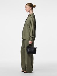 Olijfgroene, loszittende blouse met knoopsluiting aan de voorkant en een borstzak; bijpassende wijde broek. Kleine zwarte handtas met een handvat.