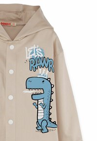 Felpa beige con una grafica frontale che presenta un dinosauro cartone animato blu. Ha un cappuccio, chiusura a bottoni e un testo giocoso "Let's PAWR."