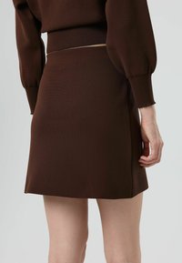 Bruine gebreide rok met een aangesloten taille en een licht uitlopende zoom. Soepele textuur en minimale details, geschikt voor casual dragen.