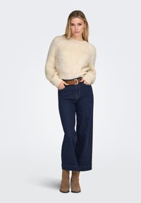 Cream, fluffy sweater with long sleeves, paired with high-waisted, wide-leg dark denim jeans. Complete with a brown belt and tan ankle boots.