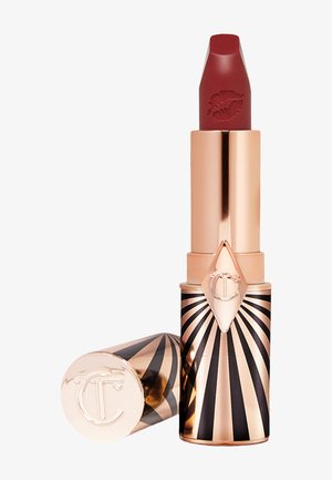 Red lipstick in a rose gold tube with black and white striped design, embossed lips on the bullet, featuring a diamond-shaped logo.