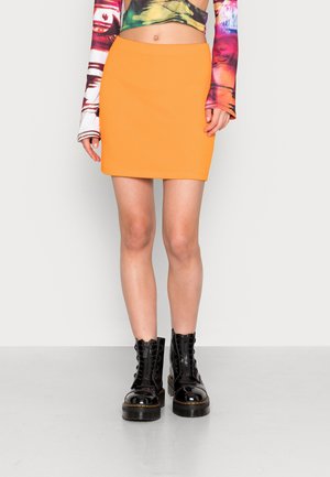 Vrouw die een feloranje minirok draagt, gecombineerd met zwarte veterlaarzen en een kleurrijke, crop top met lange mouwen.