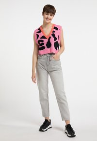 V-hals ærmeløs pink striktop med sort abstrakt mønster, parret med grå højtaljede jeans og sorte sportssko.