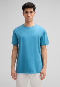 T-shirt en coton bleu à manches courtes, col rond et texture subtile. Présente un ourlet courbé et des détails de couture visibles.