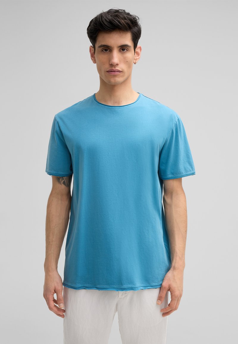 T-shirt en coton bleu à manches courtes, col rond et texture subtile. Présente un ourlet courbé et des détails de couture visibles.