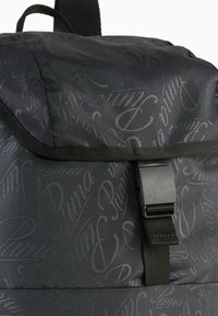 Sac à dos noir avec une finition texturée présentant un motif répétitif de "Puma" dans un design brillant. Comprend une sangle en toile noire et une boucle.
