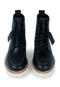 Botas de cuero negro con tobillo alto, punta redonda, suela de goma blanca y costuras en contraste. Presentan cordones y un bucle para tirar.