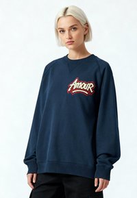 Sweat-shirt bleu marine à col rond en coton avec un ourlet côtelé, présentant un motif brodé « Amour » en rouge et beige sur la poitrine.