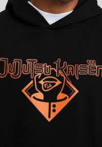 Felpa nera con cappuccio con testo grafico arancione "JuJutsu Kaisen" e logo, con linee spesse e una forma a diamante che circonda un disegno di mano.