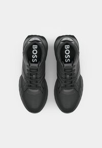 Sorte atletiske sko med en glatt skinnoverdel, gummisåle, snørelukking og "BOSS"-logo på tungen og innersålen.
