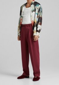 Camicetta a maniche corte multicolore con design astratto, canottiera bianca a costine, pantaloni bordeaux e scarpe slip-on in velluto abbinate.