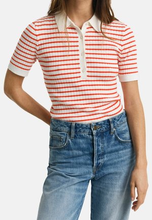 Rød- og hvidstribet ribbet polo shirt med hvid krave og korte ærmer, parret med lyseblå denimjeans. Detalje med knaplukning.