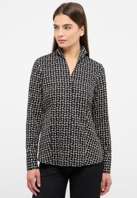 Schwarz- und cremefarbige Bluse mit Muster, Kragen und Knopfverschluss. Verfügt über ein strukturiertes Rautenmuster und lange Ärmel. Glattes Material.
