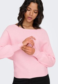 Maglione rosa chiaro a coste con scollo ampio e maniche lunghe leggermente arricciate. Presenta una fascia aderente in vita e una texture liscia.