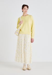 Gul genser med lange ermer, kombinert med et hvitt maxiskjørt med blomstermønster. Akkompagnert av en hekleveske og beige platåsko.