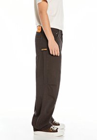 Person wearing dark pinstriped pants with a side pocket and brown sneakers with white laces, standing against a white background.