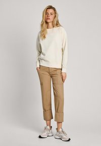 Sudadera de color beige claro con puños acanalados, combinada con pantalones cortos de color marrón claro con bolsillos tipo parche. Zapatillas en gris y blanco.