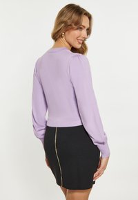 Maglione a maniche lunghe puff rosa lilla, abbinato a una gonna nera con zip dorata sul retro. Texture morbida.