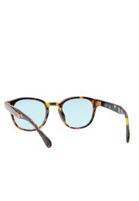 Occhiali da sole tartaruga con lenti blu, forma rotonda, montatura spessa e finitura lucida. Presentano sottili variazioni di pattern nella montatura.