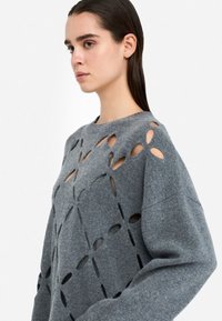 Maglione grigio a maglia con motivo floreale a intaglio, scollo rotondo e vestibilità ampia. Tessuto testurizzato con dettagli di cucitura visibili.