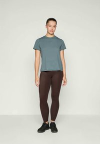 Camiseta turquesa, mangas curtas, corte descontraído. Leggings castanhas, material elástico, comprimento total. Ténis pretos, design simples.