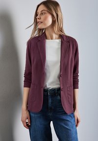 Diep paars blazer met lange mouwen, twee voorzakken en knoopsluiting, gedragen over een wit shirt en blauwe spijkerbroek.