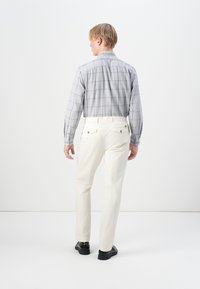 Light gray checkered shirt with long sleeves, paired with cream-colored trousers. Black footwear visible. Clean lines and structured fit.