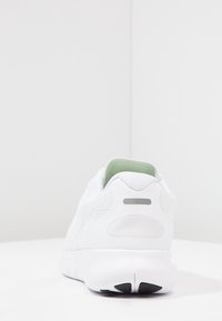 Zapatilla deportiva blanca con parte superior de malla, diseño redondeado, cuello del talón acolchado y un sutil acento gris en el talón. Suela de goma.