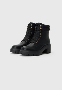 Bottines noires à talon épais, à lacets, œillets dorés et bord côtelé à la cheville. En cuir lisse avec une semelle texturée.