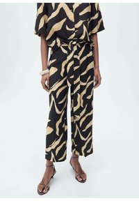 Un ensemble noir et doré avec une chemise à manches courtes et un pantalon large. Le matériau semble léger avec une texture lisse. Détail de taille nouée.