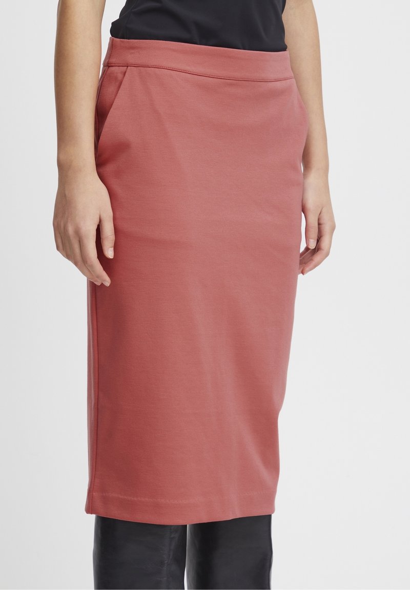 Jupe mi-longue ajustée en tissu doux de couleur rose pâle. Elle présente une large taille et des poches latérales, avec une texture lisse et des lignes épurées.