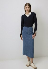 Denim midi-rok met frontsluiting met knopen, met subtiele versieringen. Gepaard met een marineblauwe trui en crèmekleurige sneakers.