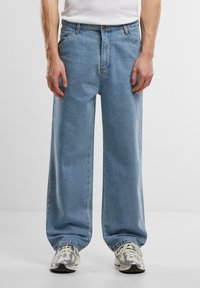 Lyseblå bredbenede jeans lavet af denim, med høj talje, fem-lomme design og syet detaljer, parret med grå sneakers.