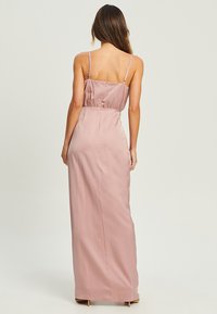 Maxi dress in soft pink satin, featuring thin adjustable straps and elastic waist, smooth texture, and a flowing silhouette.