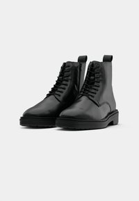 Black leather ankle boots with a rounded toe, lace-up front, and side zip. They feature a thick black rubber sole and textured upper.