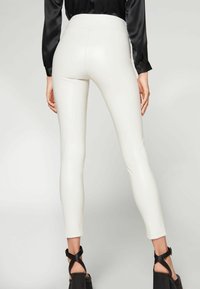 Vita figurnära leggings gjorda av ett mjukt, elastiskt material. Designen har hög midja och smala ben, i kombination med svarta klacksandaler.