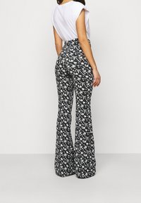 Svarta utsvängda byxor med ett vitt blommönster, med hög midja och mjukt, strukturerat tyg. Passar för olika tillfällen.