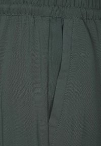 Tessuto leggero di un verde scuro con una consistenza morbida, caratterizzato da una vita arricciata e cuciture delle tasche laterali. Design minimalista.