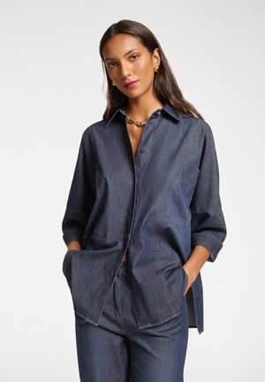 Camicia in denim blu scuro, con design a bottoni, maniche lunghe e tasche laterali. Dettagli delle cuciture e vestibilità leggermente rilassata.