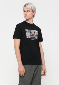Sort bomulds T-shirt med et grafisk print af vintage tv-skærme med forskellige billeder foran. Rund halsudskæring, korte ærmer.