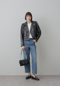 Giacca da motociclista corta in pelle nera, t-shirt bianca, jeans dritti azzurri chiaro, mocassini neri e borsa nera con tracolla a catena.