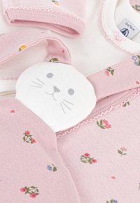 Rosa Baby-Outfit mit Blumenmustern, das ein Detail mit einem weißen Kaninchenkopf aufweist. Weicher Stoff mit strukturierten Akzenten und Pastellfarben.