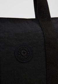 Borsa a spalla in tessuto nero con superficie testurizzata, dotata di manici in webbing neri e di un logo circolare stampato in rilievo con un design a stella.