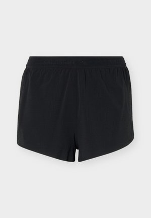 Shorts à taille élastique noire avec une coupe ample et un ourlet légèrement incurvé, présentés sur un fond gris clair uni.