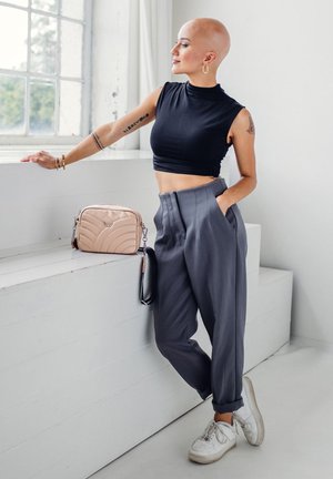Black sleeveless crop top, gray high-waisted pleated pants, white sneakers, and a light pink quilted handbag on a white surface. Natural light from window.