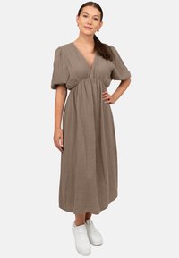 Maxi-jurk van textuur taupe stof met een diepe V-hals en pofmouwen. Draagt met witte sneakers, met een geraffineerde taille.
